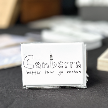 An Allara Creative card reading "Canberra — better than ya reckon" displayed on a market table.
